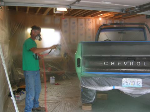 1975 Chevrolet Blazer - A person sprays paint onto a green Chevrolet pickup truck in a garage booth.