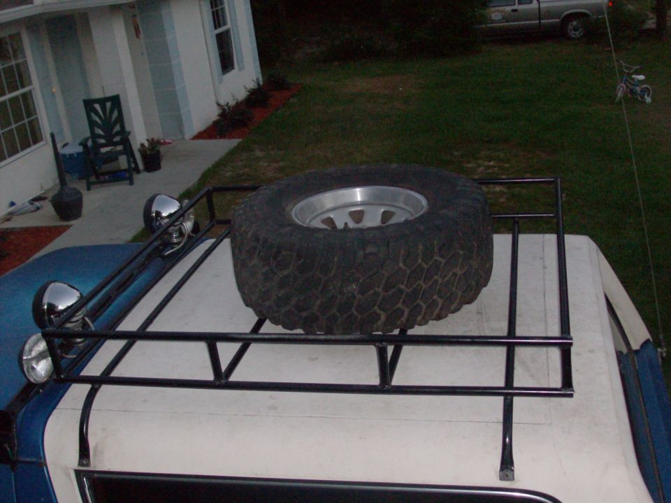 Roof rack on blue and white Bronco with spare off-road tire and chrome lights, seen from above