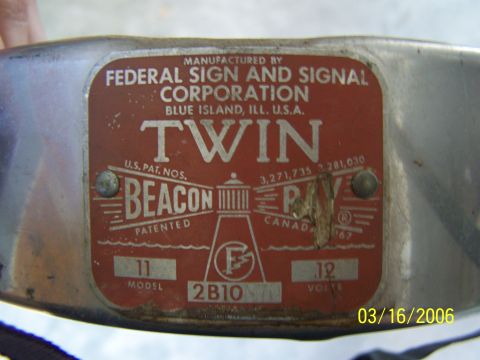 1998 Ford Crown Victoria - Close-up of the red riveted data plate on a Federal Sign and Signal Corporation 'Twin Beacon Ray' rotating warning light, mounted on a scuf…