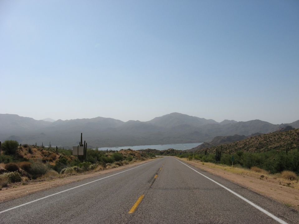 Desert highway leading to a lake with mountains in the background