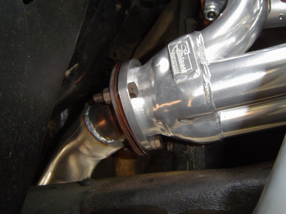 Close-up of shiny exhaust headers bolted to a flange