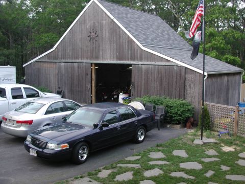 1999 Ford Crown Victoria - Dark sedan parked in front of a barn with other vehicles present.