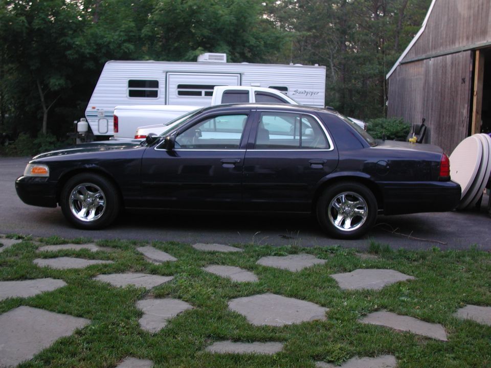 Dark sedan parked on flagstone driveway, side view. A white pickup truck and RV are behind it