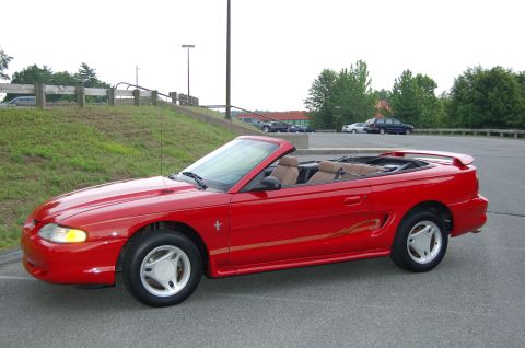 2001 Ford Crown Victoria - A red 1996 Ford Mustang convertible is parked on asphalt with a grassy embankment in the background.