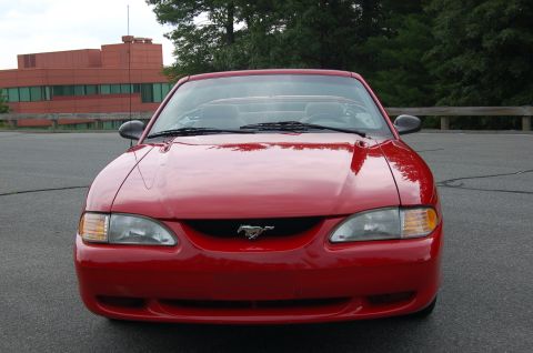 2001 Ford Crown Victoria - The front of a red convertible Mustang is shown parked outdoors with a building and trees in the background.