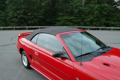 2001 Ford Crown Victoria - A red convertible is parked outdoors with trees and a wooden fence in the background.
