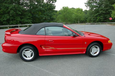 2001 Ford Crown Victoria - Side view of a red convertible Mustang with a black top and gold stripe detail.