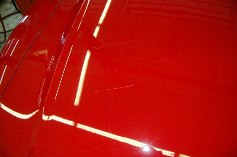 2001 Ford Crown Victoria - Close-up of a red car's hood shows several light scratches on the glossy paint surface.