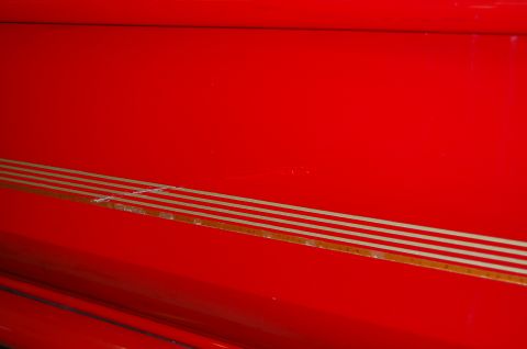 2001 Ford Crown Victoria - Close-up of a red car's side panel a decorative gold pinstripe detail.