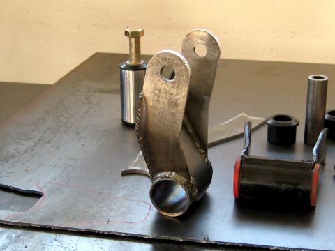 1996 Ford Bronco - Close-up of a fabricated metal suspension part with associated hardware laid out on a metal surface.