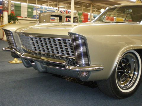 1998 Ford Crown Victoria - Close-up of the chrome grille, bumper and front fender of a silver Buick Riviera coupe at an indoor museum.