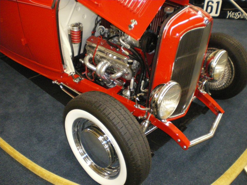 Front detail of a red hot rod roadster with chrome multi-carb engine and whitewall tire