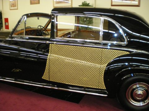 1998 Ford Crown Victoria - Side detail of a black prewar-style luxury sedan featuring a woven cane-pattern lower body panel and chrome window trim.
