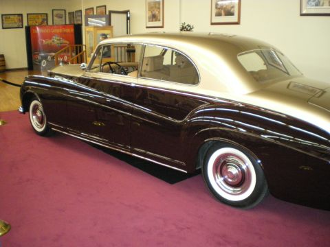 1998 Ford Crown Victoria - Two-tone maroon and gold luxury fastback sedan with whitewall tires displayed on a carpeted museum stage.