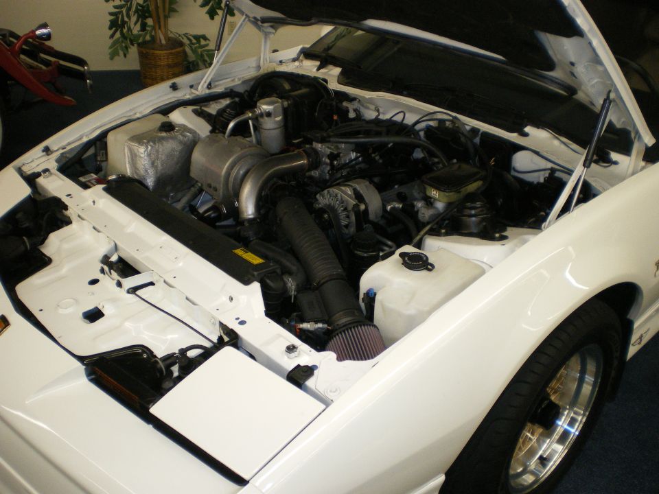 Engine bay of a white car with turbocharged engine and cone air filter, hood raised