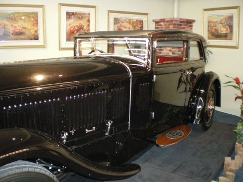 1998 Ford Crown Victoria - Dark prewar coupe shown from the side rear with a long louvered hood and side-mounted spare wheel on a display stage.