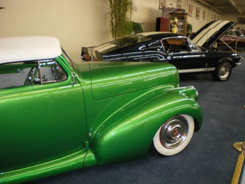 1998 Ford Crown Victoria - Green convertible with a white top displayed beside a black fastback coupe in a carpeted indoor auto collection.