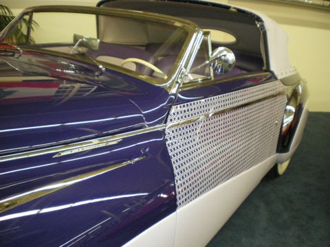 1998 Ford Crown Victoria - Close side view of a purple-over-white vintage convertible with louvered side panel and chrome spear trim indoors.