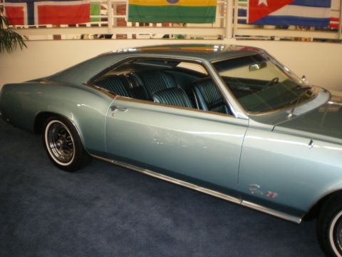 1998 Ford Crown Victoria - Side profile of a light-teal 1960s personal-luxury coupe with sweeping fastback roofline parked under flags.