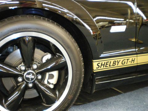 1998 Ford Crown Victoria - Close-up of a black Mustang Shelby GT-H front wheel with chrome lip and a yellow rocker stripe lettered SHELBY GT-H.