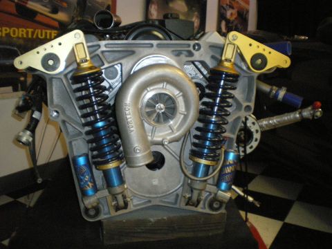 1998 Ford Crown Victoria - machined engine block on a stand displaying internals, flanked by blue twin coilover shock absorbers.