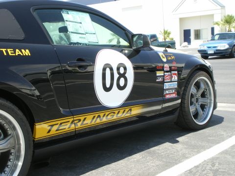 1998 Ford Crown Victoria - Side view of a black Terlingua Racing Mustang number 08 with yellow rocker stripe and sponsor decals in a lot.