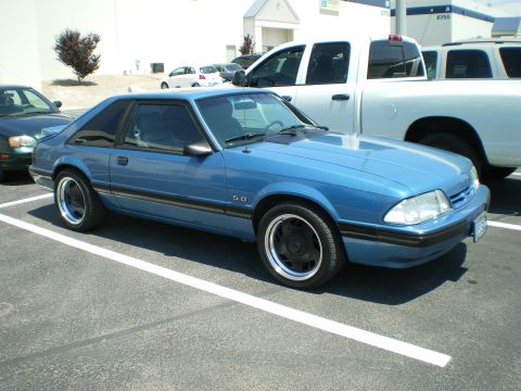 1998 Ford Crown Victoria - blue Fox-body Ford Mustang LX 5.0 hatchback on chrome wheels parked next to white pickup trucks.