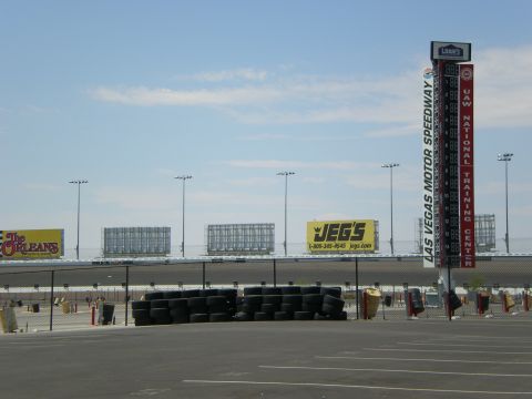 1998 Ford Crown Victoria - Stacked safety barriers and tire bundles in the Las Vegas Motor Speedway infield beneath JEGS and sponsor signage.