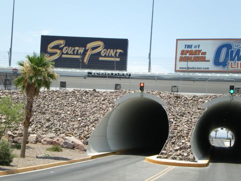 1998 Ford Crown Victoria - Two road tunnels pass under a racetrack embankment near a South Point billboard and a single palm tree.