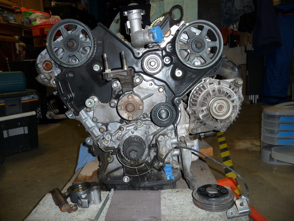 V6 engine on a stand with timing covers removed, exposing cam pulleys and crank sprocket during a timing belt job