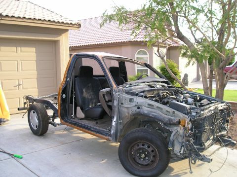 1986 Toyota Hilux - This truck chassis, missing most of its body, is parked in a driveway with the engine exposed.