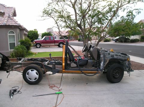 1986 Toyota Hilux - A disassembled truck chassis sits in a driveway, showing its frame and interior components. A red pickup truck is parked in the background.