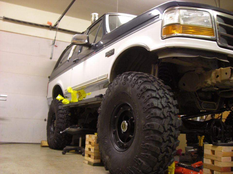 1993 Ford Bronco with oversized off-road tires, lifted and on blocks in a garage