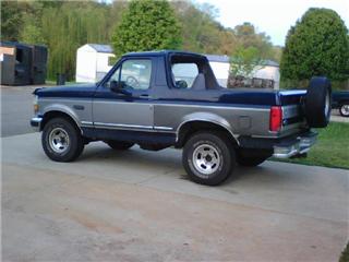 1995 Ford Bronco - This two-tone Ford Bronco is seen from a three-quarter front angle, parked on a concrete driveway with buildings in the background.