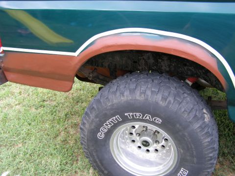 1993 Ford Bronco - The rear wheel well of a green Ford truck shows signs of rust repair and a large off-road tire.