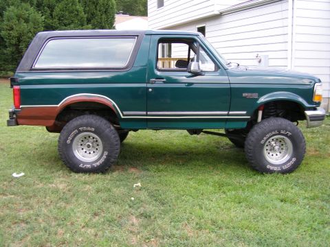 1993 Ford Bronco - Side view of a lifted green SUV with a black removable top and off-road tires.