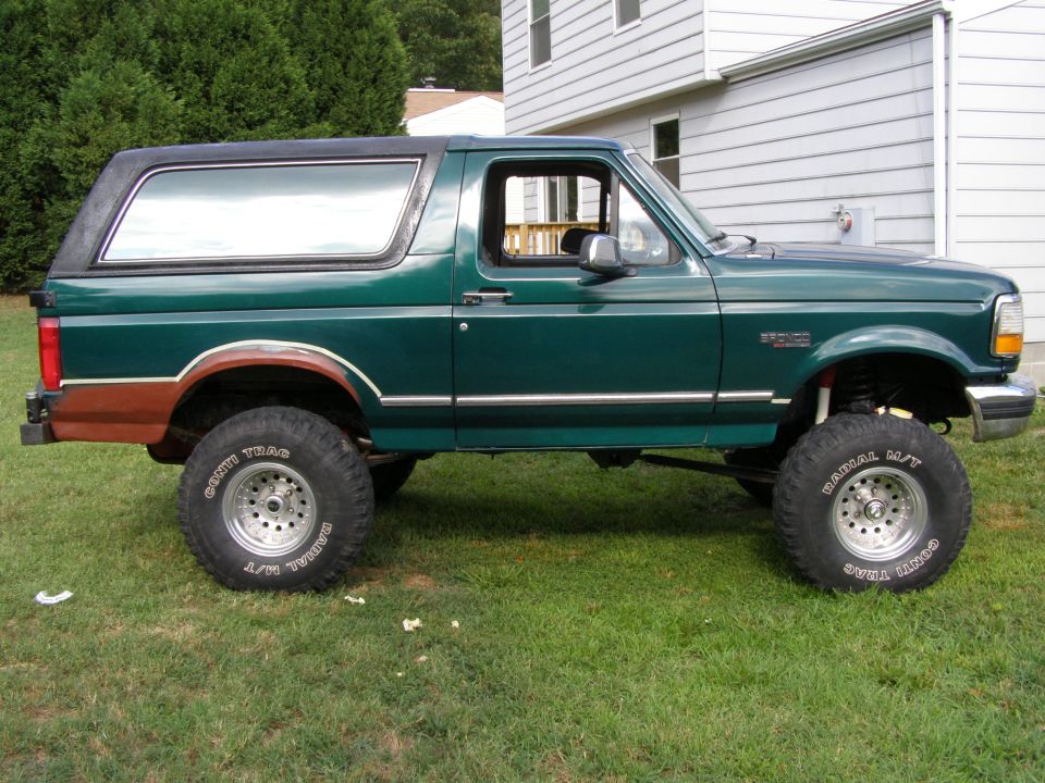 Green 1993 Ford Bronco with lifted suspension and aftermarket wheels parked on grass