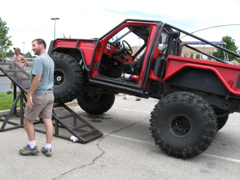 1994 Ford Bronco - A heavily modified off-road vehicle with oversized tires and a protective roll cage is positioned on a ramp at a car show.