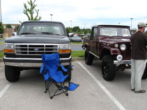1994 Ford Bronco - Two trucks, a 1994 Ford Bronco and a maroon Jeep pickup, are parked side-by-side in a lot.