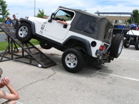 1994 Ford Bronco - A white Jeep Wrangler is positioned on a ramp at an event, with other vehicles visible in the background.