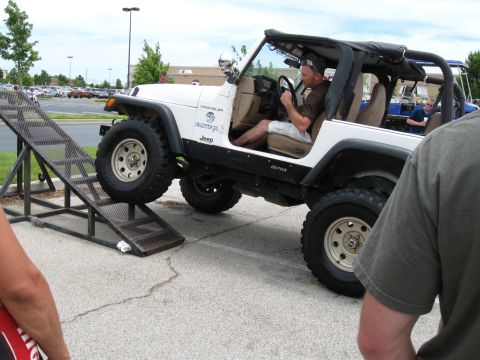 1994 Ford Bronco - A white Jeep Wrangler is shown driving up a metal ramp at what appears to be a car show.