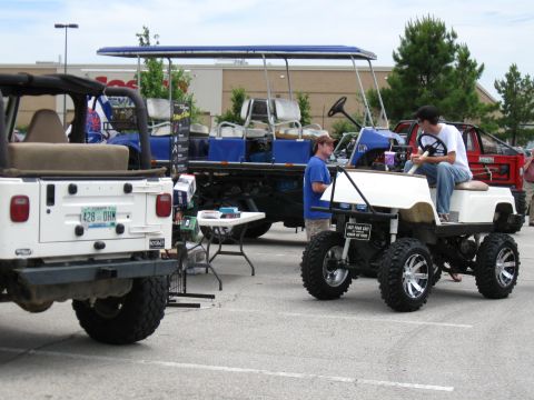 1994 Ford Bronco - A modified golf cart with custom wheels and tires is displayed at an outdoor event.