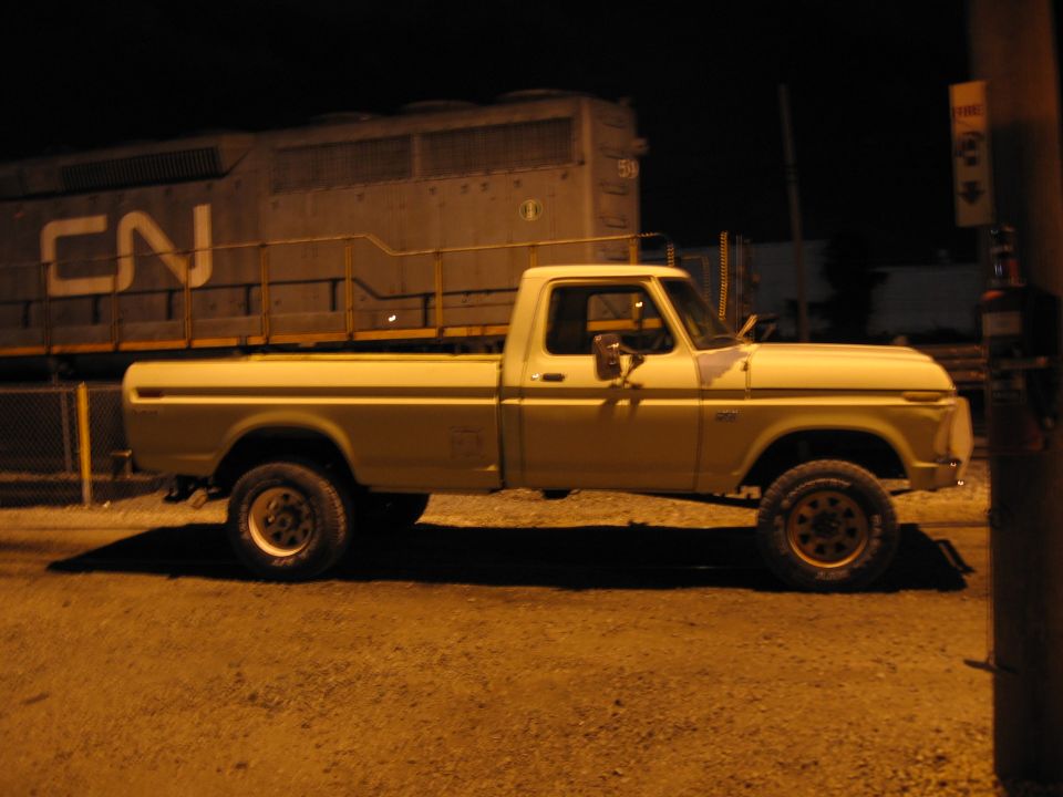 Cream 1970s Ford F-series long-bed pickup at night in front of a CN diesel locomotive