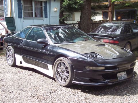 1995 Ford Probe - A modified black Ford Probe with a grey hood and custom body kit is parked outside a trailer home.