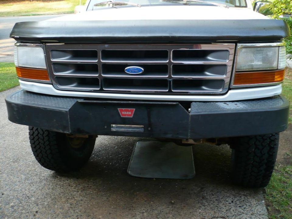 Front of a Ford truck with a chrome grille, amber turn signals, and a black aftermarket bumper with a WARN winch plate
