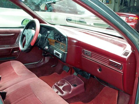 1989 Ford Thunderbird - The interior of a car shows red upholstery and a dashboard with wood trim details.