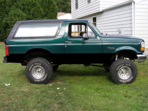 1993 Ford Bronco - A lifted green and black Ford Bronco is parked on a grassy lawn next to a house.