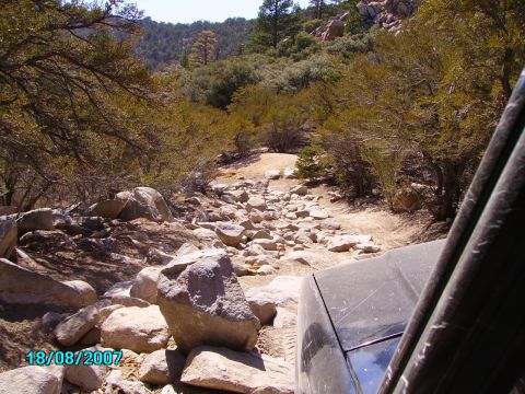 1990 Ford Bronco - A vehicle navigates a rough, boulder-strewn path through a dry, wooded landscape.