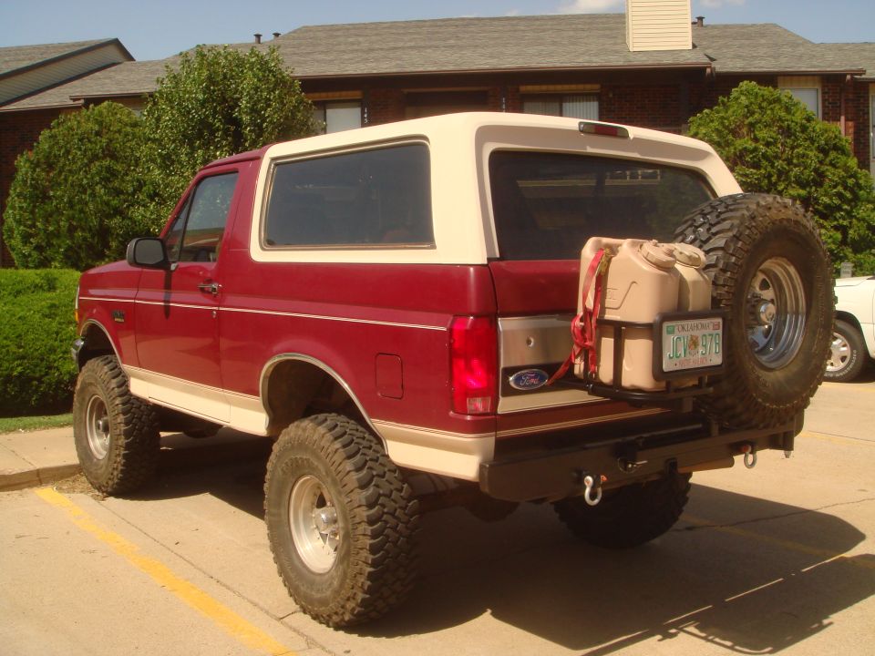 Lifted red and cream Ford Bronco, 3/4 rear, with spare carrier and tan jerry cans