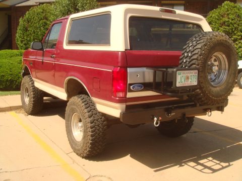 1992 Ford Bronco - Rear three-quarter view of a lifted maroon Ford Bronco with a white removable hardtop and tan lower two-tone, parked on a concrete lot in f…